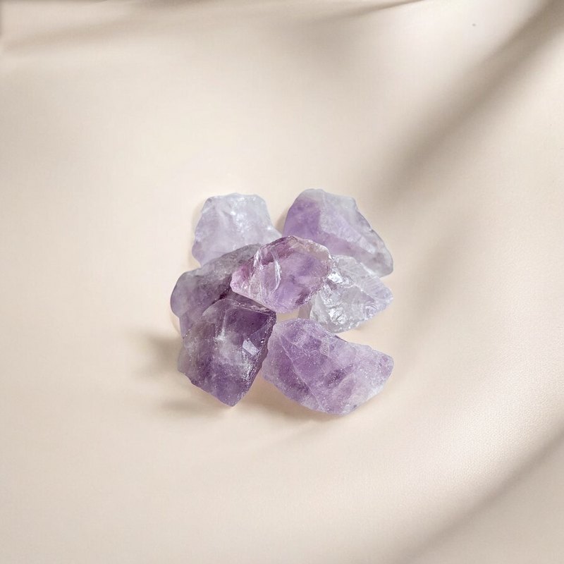 Raw Amethyst crystals in soft to medium purple hues with natural clarity, photographed on a creamy blush background