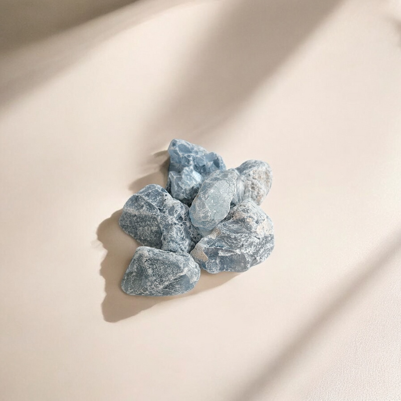 Raw Celestite crystals in soft sky blue tones with natural texture and matte finish, photographed on a light cream beige background