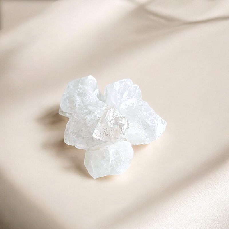 Raw Clear Quartz crystals with transparent clarity and natural facets, photographed on a soft cream-toned background