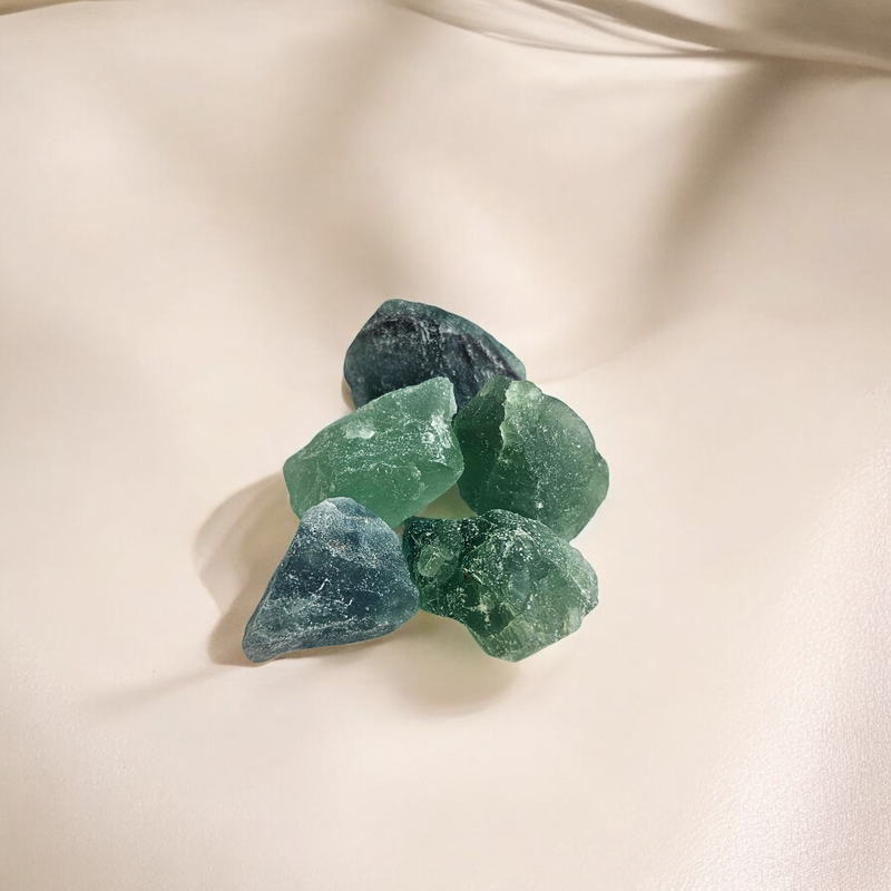 Raw Green Fluorite crystals in translucent forest and seafoam green shades, photographed on a soft beige background