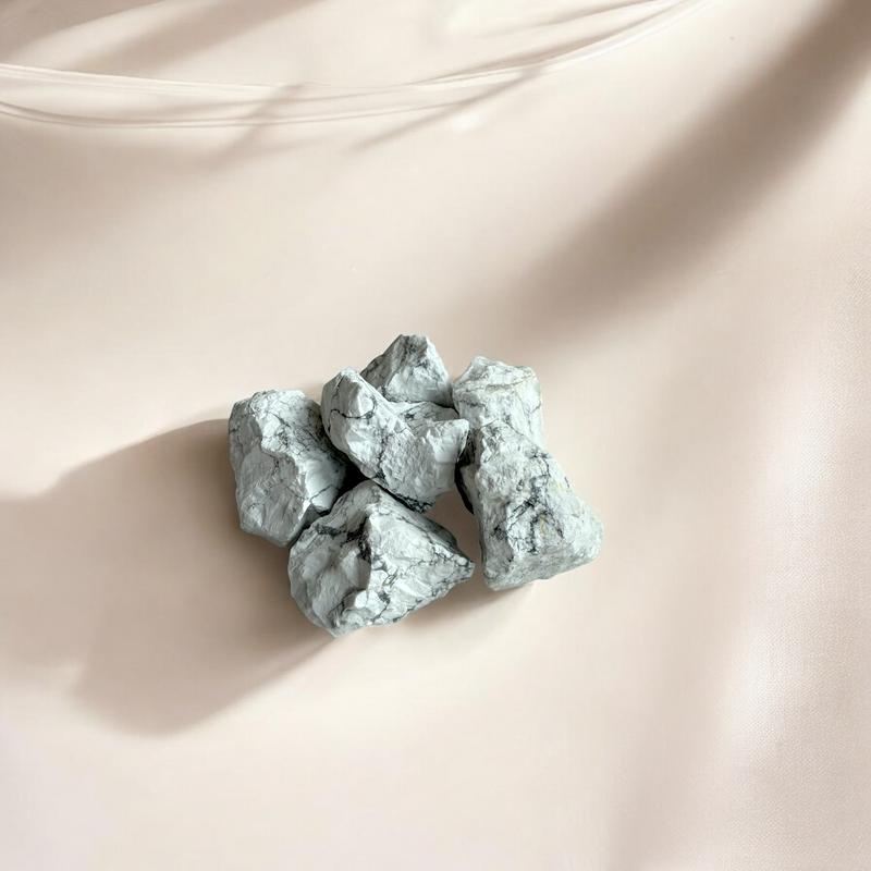 Raw Howlite crystals in soft white with natural grey veining, photographed on a light blush background