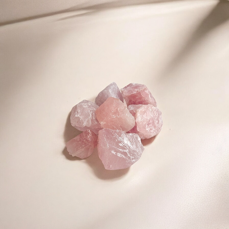 Raw Rose Quartz crystals in soft pink tones with a gentle shimmer, photographed on a light cream background