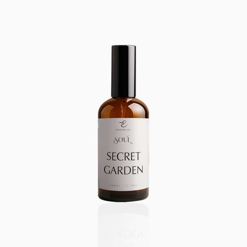 100ml Secret Garden fragrance mist in amber glass bottle with black cap and soft pale pink label, photographed on white background