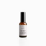 50ml Secret Garden fragrance mist in amber glass bottle with black cap and soft pale pink label, photographed on white background