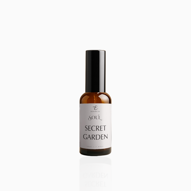 50ml Secret Garden fragrance mist in amber glass bottle with black cap and soft pale pink label, photographed on white background
