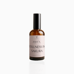 100ml Stillness In Sakura fragrance mist in amber glass bottle with black cap and blush pink label, photographed on white background