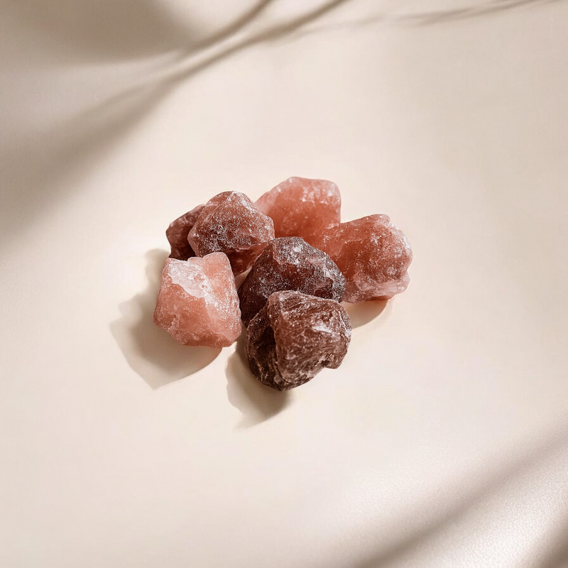 Raw strawberry quartz crystals in shades of dusky pink and deep rose, lightly frosted in texture and arranged on a soft beige surface with gentle shadow play