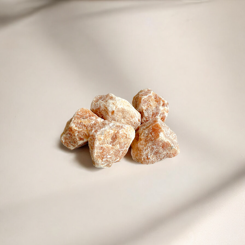 Raw Sunstone crystals in warm terracotta-orange tones with a dusty, matte texture, arranged on a soft beige surface with gentle shadows